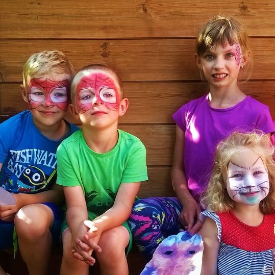 Photo of four kids with face paing on. They are happy. Two are painted like spiderman, one like a cat, and the last one has a fun design on her face.