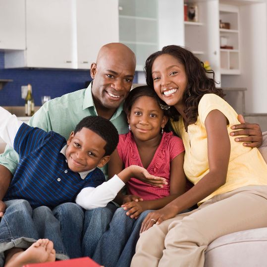 photo of a black family of four on a couch looking happy.